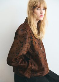 Brown bomber jacket with black spots, featuring a zip closure and ribbed cuffs. Material appears textured and soft.