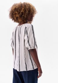 Losse witte blouse met zwarte verticale strepen, geweven stof, ballonmouwen en kantdetails bij de mouwboorden.