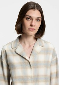 Plaid shirt in soft fabric, featuring blue and beige colors, buttoned front, notched collar, and embroidered logo on left side.