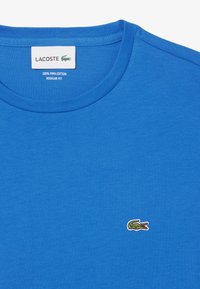 Camiseta azul de corte regular hecha de 100% algodón pima, con un pequeño logo de cocodrilo verde bordado en el pecho. Textura suave.