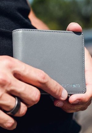Gray leather wallet with smooth texture, rectangular shape, and logo detail. Held in a hand, showcasing its slim profile.