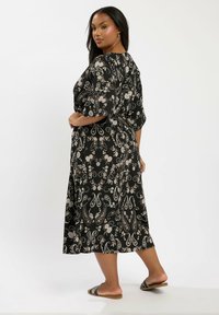 Musta paisley-kuvioinen mekko, jossa on lyhyet hihat, polvimittainen helma ja rento malli. Yhdistetty ruskeisiin liukujalkineisiin, joissa on valkoisia yksityiskohtia.