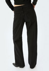 Pantalones de pierna ancha a rayas negras con cintura alta, que cuentan con bolsillos traseros de parche y una textura suave. El diseño ajustado acentúa la forma.