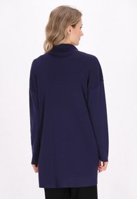 Maglione a maniche lunghe con collo alto di un blu scuro, realizzato in un tessuto morbido con vestibilità ampia, caratterizzato da un alto colletto e spalle scese.