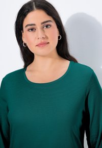 Zielona koszula z długim rękawem i okrągłym dekoltem, wykonana z gładkiego materiału. Charakteryzuje się delikatną teksturą i dopasowaną sylwetką.