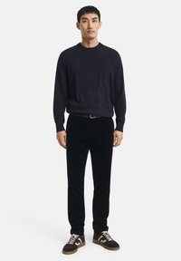 Pull en tricot bleu marine foncé avec un col rond, accompagné de pantalons en velours côtelé noirs. Les chaussures présentent des accents marron foncé et blancs.