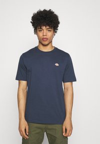 T-shirt de algodão azul-marinho com gola redonda, mangas curtas e um pequeno logotipo laranja no peito. Apresenta um corte clássico e uma textura suave.