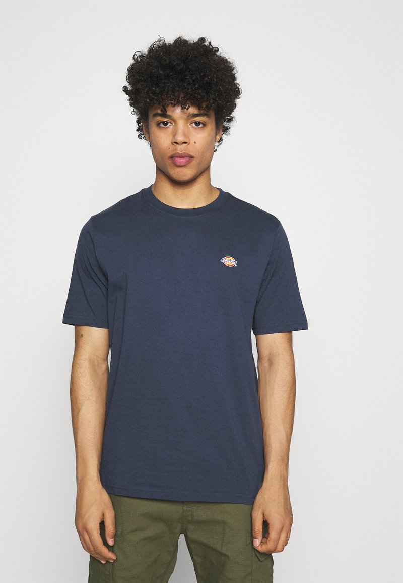 T-shirt de algodão azul-marinho com gola redonda, mangas curtas e um pequeno logotipo laranja no peito. Apresenta um corte clássico e uma textura suave.