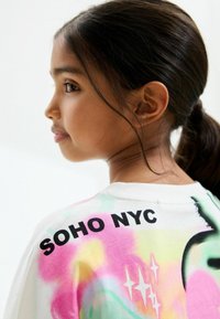 T-shirt en coton blanc avec des éclaboussures colorées en rose, jaune et vert. Le texte au dos dit "SOHO NYC" en lettres noires en gras.
