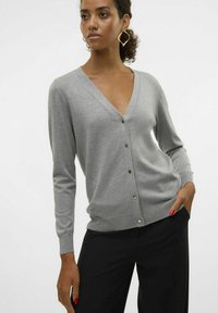 Grå cardigan med V-ringning, figursydd design, långa ärmar och guldknappdetaljer. Tillsammans med svarta byxor. Slät textur.