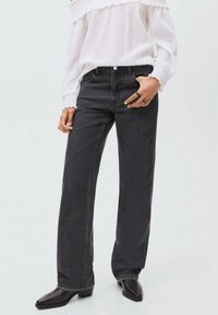 Svarta vida jeans med en texturerad yta, med knappstängning och kontraststickning, kombinerat med en vit blus och svarta ankelboots.