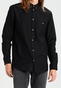 Zwarte button-up shirt gemaakt van katoen, met een klassieke kraag, een zak aan de linkerkant en zilverkleurige knopen. Lange mouwen met manchetten.