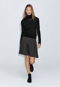 Maglione a collo alto nero, gonna plissettata grigia e scarpe slip-on nere. Tessuto liscio, design aderente e leggere variazioni di texture.