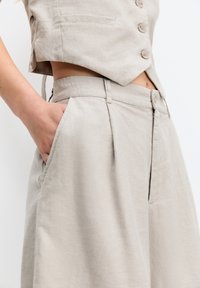 Ensemble en lin beige comprenant un haut à manches courtes avec boutons et un pantalon taille haute à jambes larges, mettant en valeur de subtils plis et des poches latérales.