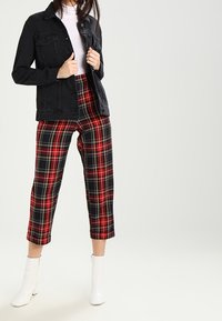 Black denim jacket over a white turtleneck, paired with red and black plaid cropped pants and white ankle boots.