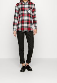 Rød, grøn og hvid ternet flannel skjorte med krave og brystlomme, parret med sorte bukser og sorte loafers.