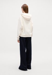 Felpa color crema con cappuccio regolabile, abbinata a jeans ampi blu navy. Tessuto liscio con polsini e vita a costine.