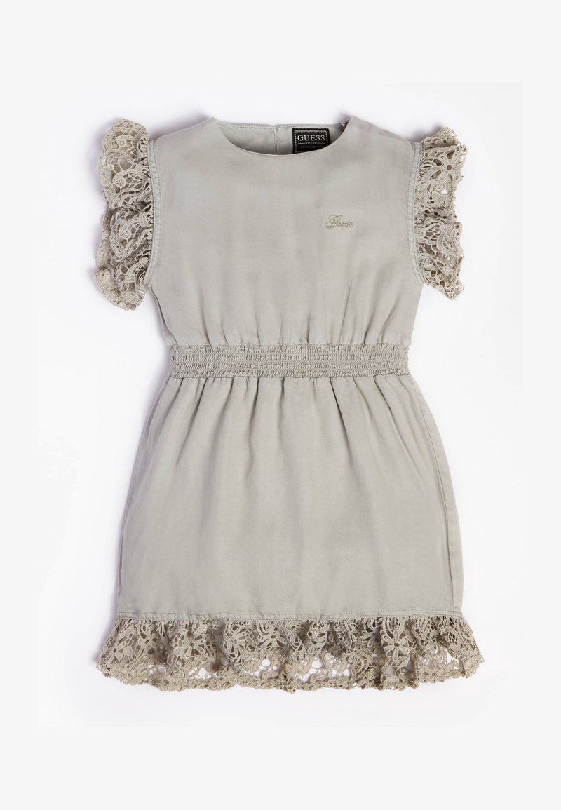 Robe beige clair sans manches avec volants en dentelle aux manches et à l'ourlet, taille élastiquée froncée et petit logo Guess brodé sur la poitrine.