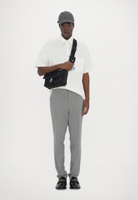 Camicia bianca a maniche corte con taschino; pantaloni grigi a quadri; borsa a tracolla nera; cappellino grigio; mocassini neri con dettaglio a catena.