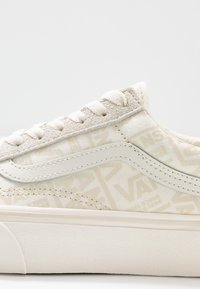 Zbliżenie beżowego i białego sneakersa Vans z teksturowanymi sznurowadłami, zamszową panelą wokół oczek i subtelnym wzorem logo Vans na górnej części z tkaniny.