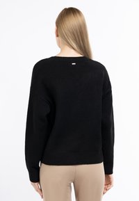 Black knitted sweater with a relaxed fit, ribbed cuffs, and hem. Minimalist design with a white tag near the neck, smooth texture.