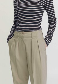 Gestreepte lange mouwen top in marineblauw en beige, gecombineerd met licht kaki plissébroek met zijzakken en een knoopsluiting.