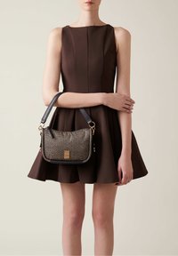 Borsa nera e oro con superficie strutturata, forma rettangolare e tracolla nera staccabile, appoggiata su un vestito marrone.