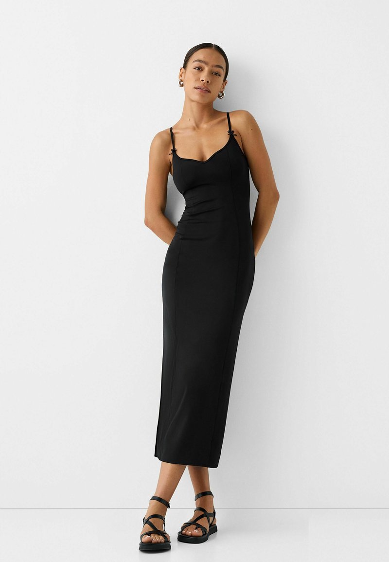 Vestito nero a sottoveste con spalline sottili, una silhouette aderente e lunghezza fino al polpaccio. Tessuto morbido, con spacchi laterali per facilitare il movimento.