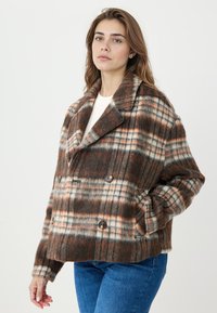 Veste en laine marron à carreaux avec boutons croisés, larges revers et poches latérales. Le motif comprend des accents orange et crème.