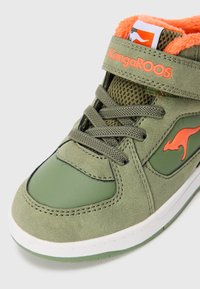 Grønn og oransje KangaROOS-sneaker med snøring, borrelås, mesh-tunge, kenguru-logo og oransje fleece-fôr, vist fra forsiden.