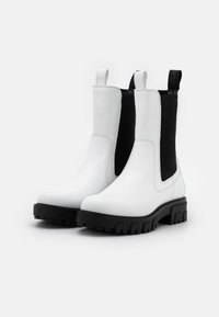 Botas de tobillo de cuero blanco con paneles laterales elásticos negros, puntera redondeada y suela gruesa de goma negra con textura para agarre.