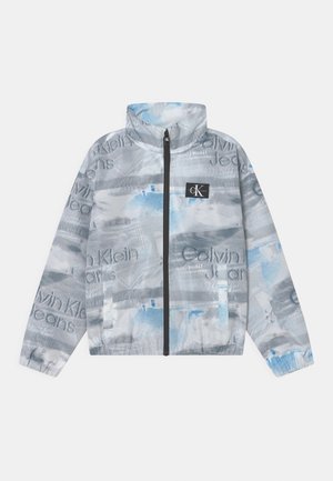 Chaqueta gris claro con cremallera, con patrones abstractos en azul y blanco, parche con el logo de Calvin Klein Jeans en el pecho, y puños y bajo elásticos.
