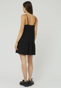 Robe noire sans manches avec une taille froncée, un ourlet à volants et une texture côtelée, associée à des chaussures noires à lacets. Design simple et décontracté.