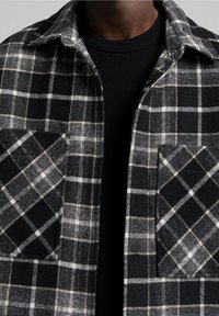 Svart och vit rutigt flanellskjorta med två framfickor, med en knäppdesign och en mjuk textur. Lagd över en svart tröja.