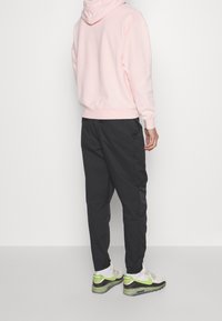 Ljust rosa hoodiesweatshirt, svarta byxor och flerfärgade sneakers. Hoodien har en avslappnad passform med en kenguruficka; sneakers har gröna detaljer.