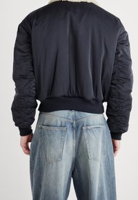 Chaqueta bomber de la marina con cuello de piel sintética, puños y cintura acanalados, combinada con jeans de mezclilla desgastados de color azul claro con grandes bolsillos traseros.