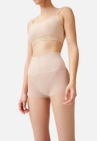 Nahtloses Set aus BH in Nude und hochgeschnittenen Shorts. Weich, elastischer Stoff mit glatter Textur. Verstellbare Träger und Logo-Banddetails.