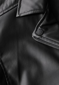 Veste en simili cuir noir avec fermeture éclair, détails à boutons-pression, accents matelassés et texture lisse.