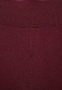 Bordeaux leggings met een geribbelde textuur en een brede, elastische tailleband. De stof lijkt zacht en iets rekbaar te zijn.