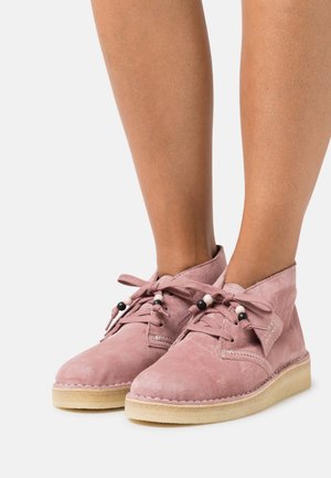 Bottines en suédine rose poussiéreux avec bouts ronds, lacets en tissu et perles décoratives. Semelle en caoutchouc texturé et détails cousus.