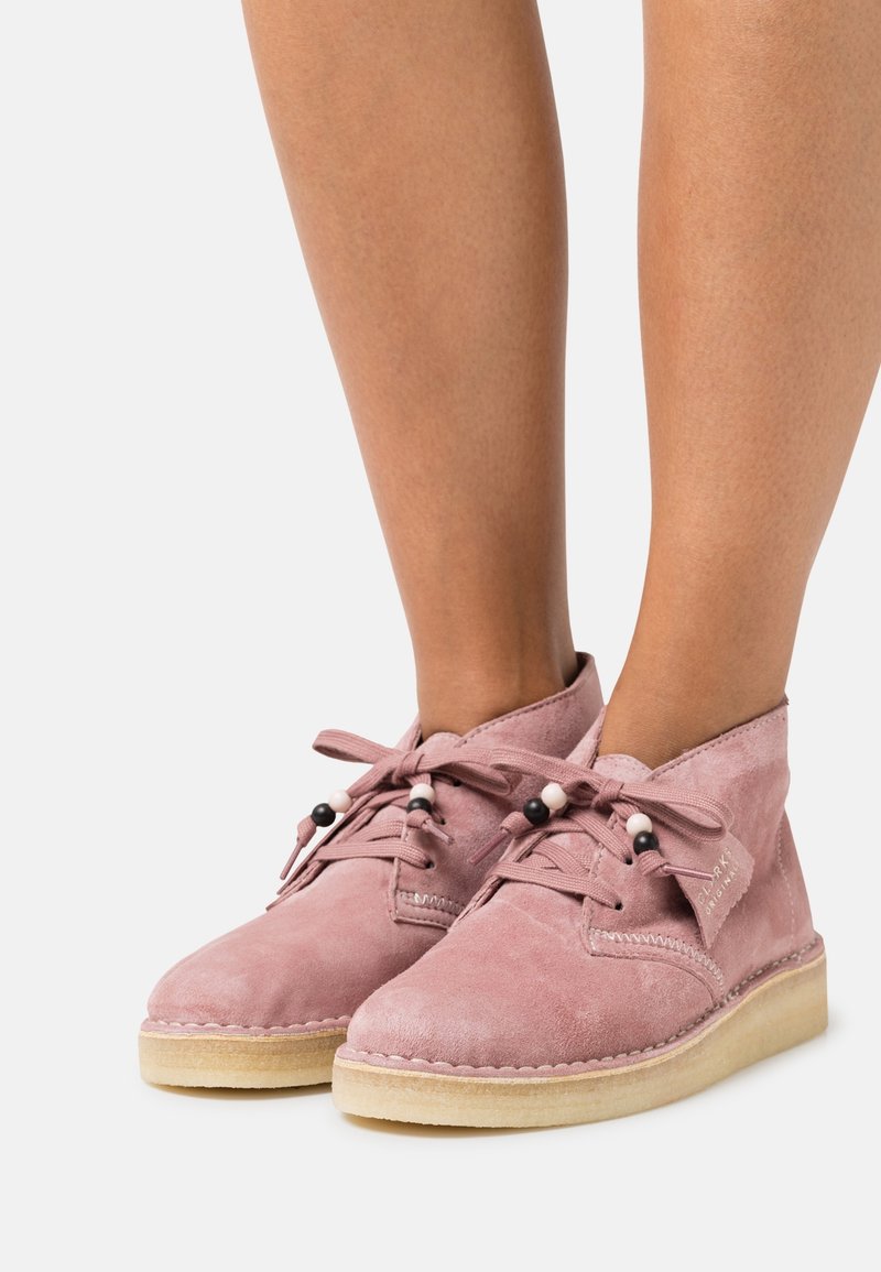 Botas de tobillo de ante rosa empolvado con punteras redondas, cordones de tela y cuentas decorativas. Suela de goma texturizada y detalles cosidos.