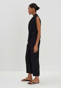 Haut sans manches noir avec un nœud à la taille, associé à un pantalon noir à jambes larges et des sandales plates, avec une texture lisse.