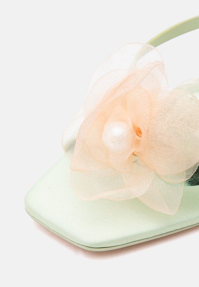 Κοντινό πλάνο ανοιχτόχρωμου πράσινου σανδάλου με διαφανές ροδακινί υφασμάτινο λουλούδι και κεντρικό διακοσμητικό από μαργαριτάρι στο λουράκι.