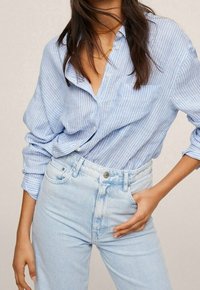 Camisa de botón a rayas azul y blanca con un corte relajado, combinada con jeans de tiro alto en azul claro. El tejido parece suave y transpirable.