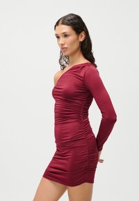 Vynio su viena petneša bordo spalvos su ilgomis rankovėmis, pasižyminti raukšlių detalėmis ir prigludusia siluetu, pagaminta iš elastingos medžiagos.