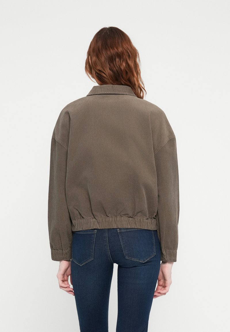 Veste en velours côtelé marron, courte, avec un col, une taille élastique et des manches longues. Texture simple avec un motif fin de plis.