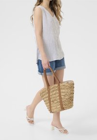 Woven straw tote bag z brązowymi skórzanymi uchwytami; wysoki prostokątny kształt; naturalny kolor z skomplikowanym wzorem; nosi się swobodnie.