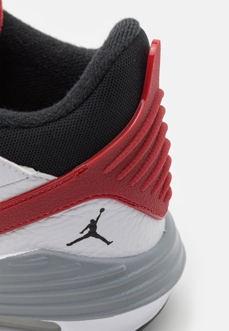 Zapatilla de cuero blanca con acentos rojos, cuello de tela negra texturizada y suela de goma gris. Presenta el logo negro de Jumpman en el costado.
