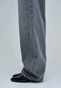 Jeans de mezclilla gris de pierna ancha con un ajuste holgado, que presentan un sutil efecto de desgaste y se combinan con botas negras de tacón puntiagudas.