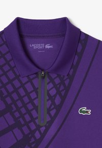 Paarse polo met ritskraag, voorzien van een geraamd patroon en contrasterende donkerpaarse accenten. Inclusief een Lacoste-logo op de borst.